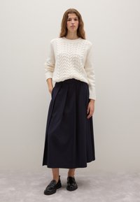 White knitted sweater with cable pattern, paired with a knee-length navy skirt featuring pleats, and black loafers. Smooth textures throughout.