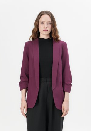 Burgundy blazer with notched lapels and three-quarter sleeves, paired with a black ribbed top, featuring a scalloped neckline.