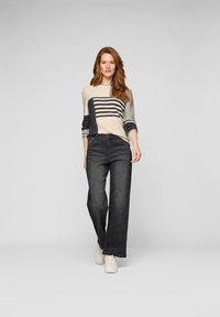 Strickpullover mit horizontalen Streifen in Beige und Grau, kombiniert mit weit geschnittenen dunkelblauen Jeans und weißen Turnschuhen. Einheitlicher Hintergrund.