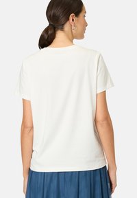 White cotton t-shirt with short sleeves, crew neckline, and a plain back design, paired with a blue pleated skirt.