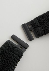 Svart elastisk håraccessoar med samlad textur, robust svart hårdvara och en spänndesign för säker användning.