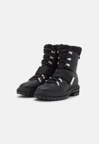 Botas de invierno negras de cuero con un cuello de forro polar texturizado negro, herrajes plateados y una suela de goma gruesa para mayor tracción.