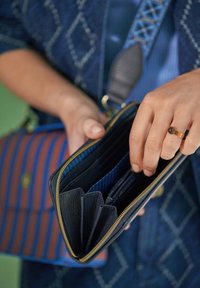 Black leather wallet with gold zipper, multiple compartments, and blue striped interior, being held by a hand with a ring.