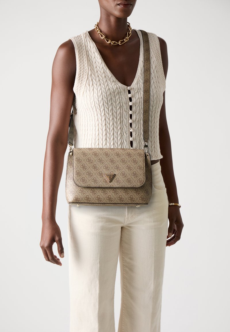 Borsa a tracolla beige con motivo, chiusura a patta, hardware logo dorato e tracolla texture. Indossata con un top senza maniche in maglia e pantaloni bianchi.