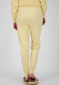 Gele joggers met een zachte textuur, taperende pijpen en een elastische tailleband, gedragen met lichtgekleurde instapschoenen met een jute zool.