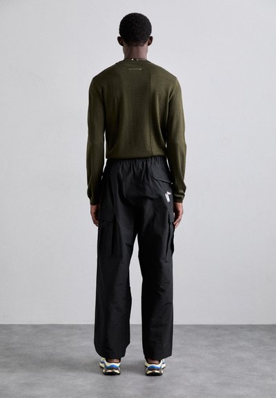 Olivenfarget strikkegenser med rund hals; svarte cargo-bukser med flere lommer; uformelt fottøy med blå og hvite detaljer.