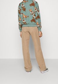 Chaqueta bomber floral verde menta con puños acanalados, combinada con pantalones de pana beige de pierna ancha y zapatillas en blanco y negro.