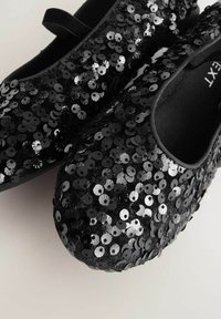 Bailarinas negras cubiertas de lentejuelas negras y plateadas, con punta redondeada y una pequeña correa negra en el talón. Textura suave.