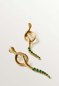 Pendientes en forma de serpiente dorada con escamas texturizadas y acentos de piedras de color verde esmeralda. El diseño presenta una forma retorcida con elementos circulares.