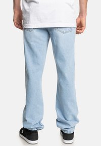 Helle blaue Denim-Jeans mit lockerer Passform, sichtbaren Nähten und standardmäßigen Gesäßtaschen. Kombiniert mit schwarzen Sneakern.