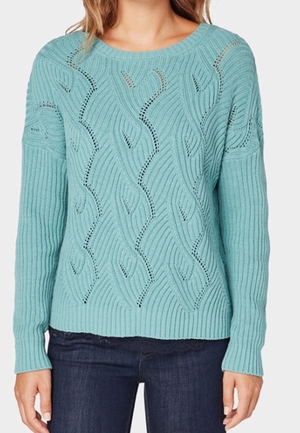 Pull bleu clair en tricot avec une texture côtelée, présentant des motifs ondulés et des détails en ajouré. Col rond et manches longues.