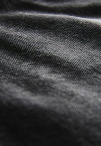 Tela negra con una superficie texturizada, que presenta sutiles variaciones en sombra y patrón, mostrando pliegues y arrugas.