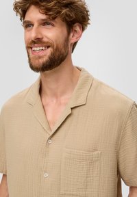 Beige overhemd met korte mouwen van textuur-katoen, voorzien van een zak, een kraag en vijf knopen. De stof heeft een subtiel kreukpatroon.