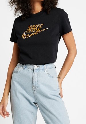 T-shirt noir en coton avec un logo Nike imprimé léopard, associé à un jean en denim bleu clair taille haute. Coupe droite et manches courtes.