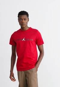 Rød bomulds t-shirt med stor sort "JORDAN" tekst og logo i midten. Korte ærmer, rund halsudskæring og en glat tekstur.
