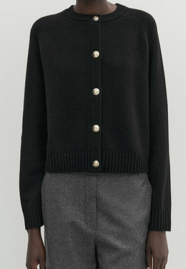 Cardigan en maille noir à manches longues avec six boutons dorés, associé à un pantalon en laine gris taille haute.
