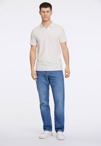 Kremfärgad pikétröja med korta ärmar, lätt material, ihopparad med blå jeans och vita sneakers. Enkel design, inga synliga mönster.