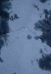 Niebieska bawełniana tkanina z wzorem tie-dye w ciemniejszym odcieniu niebieskiego i szarości. Posiada ukośny szew z wyraźnym detalem szycia.