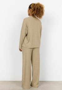 Beige gerippter Strickoberteil und weit geschnittene Hose, die eine lockere Passform, lange Ärmel und einen strukturierten Stoff aufweist. Glatte Oberfläche mit vertikalen Streifen.