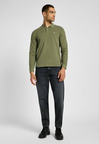 Olivgrön långärmad polo skjorta med en kontrasterande vit krage, matchad med mörka jeans och svarta läderstövlar.