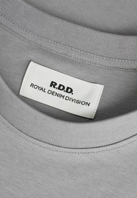 Pelēkokas kokvilnas t-krekls ar apaļu kakla izgriezumu. Iezīmēts ar detalizētu šuvju izpildījumu un auduma birku ar uzrakstu "R.D.D. ROYAL DENIM DIVISION" melnā krāsā.