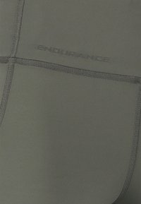 Tumma harmaa urheilukangas, jossa on sileä pinta, koristeltuna ommelluilla saumoilla ja kohokuvioidulla brändinimellä "ENDURANCE" pinnassa.