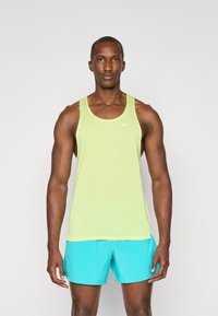 Débardeur Nike vert citron en tissu respirant, à encolure ronde et sans manches, associé à un short de sport turquoise.