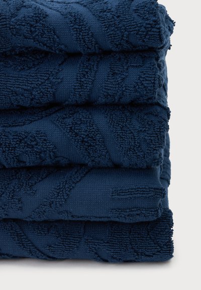 Pile de quatre serviettes bleu foncé pliées avec des motifs texturés sur un fond clair uni.