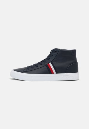 Baskets montantes noires avec semelle blanche et bandes latérales rouges, blanches et bleues, munies de lacets noirs et d’un logo embossé sur la semelle.