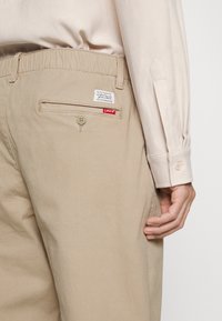 Beige broeken met elastische tailleband, voorzien van een achterzak met een knoop en een Levi's merketiket. Soepele katoenstof.