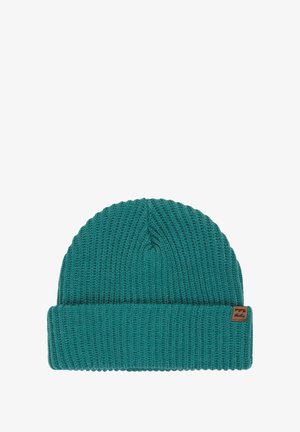 Smaragdgroene gebreide beanie met een geribbelde textuur, voorzien van een opgerolde boord en een klein bruin merklabel aan de zijkant.