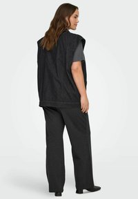 Zwarte denim bodywarmer met wijde armsgaten, achterkant met stukadoordetail en een rechte snit, gecombineerd met donkergrijze wijde broekspijpen en zwarte enkellaarsjes.