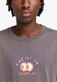Camiseta de algodón gris con un estampado gráfico que presenta dos ojos y el texto "ELEMENT SKATE CO." en varios colores. Diseño de cuello redondo.