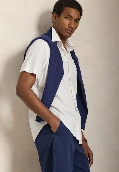 White textured short-sleeve shirt paired with a dark blue knitted sweater draped over shoulders, and navy blue trousers, all casual wear.