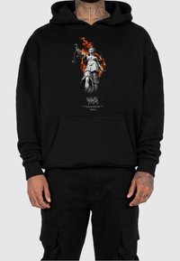 Felpa nera con cappuccio con una grafica centrale di una donna che tiene una bilancia tra le fiamme, dotata di tasca a marsupio e polsini a costine.