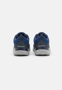 Sapatilhas de atletismo azul-marinho com parte superior em malha, colarinho acolchoado, alça de puxar e sola de borracha cinza. Apresenta o logotipo "SKECHERS" no calcanhar.