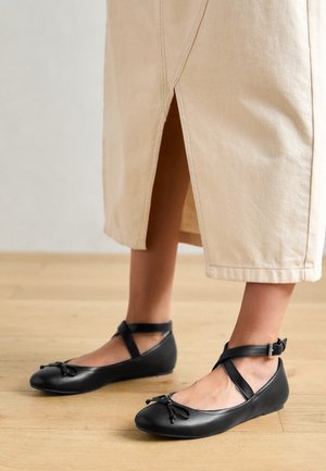 Czarne skórzane baletki z zaokrąglonym noskiem, paskiem wokół kostki i detalem w formie kokardy z przodu. Gładka tekstura, minimalistyczny design.