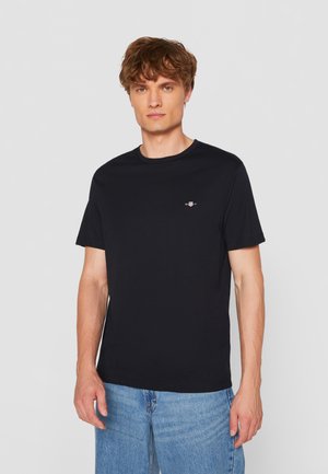 T-shirt in cotone nero con collo rotondo, maniche corte e un piccolo logo sul petto. Abbinato a jeans in denim blu chiaro.