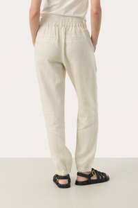 Lightweight, cream-colored trousers with an elastic waistband and gathered ankle cuffs, featuring two back pockets and a relaxed fit. Worn with black sandals.