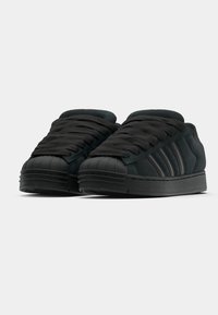 Czarne zamszowe sneakersy z gumowym czubkiem, płaskimi sznurowadłami i trzema czarnymi paskami po boku. Niska sylwetka z teksturowaną powierzchnią.