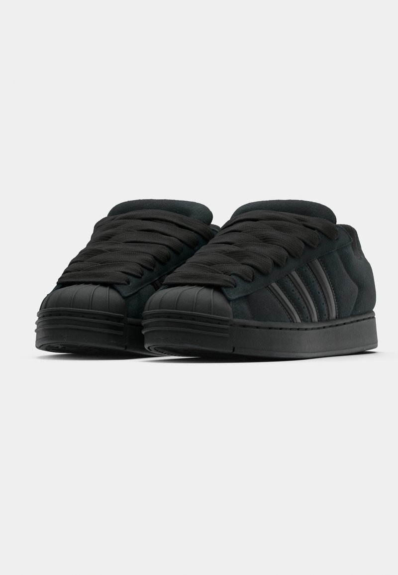 Baskets en daim noir avec embout en caoutchouc, lacets plats et trois bandes noires sur le côté. Design profil bas avec surface texturée.