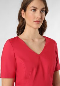 Czerwona sukienka na krótki rękaw z dekoltem w kształcie litery V, wykonana z gładkiego materiału, z delikatnymi szwami i krojem, tworzącym zarysowane sylwetki.