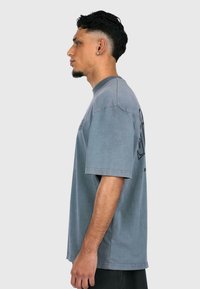 Gray cotton t-shirt with short sleeves, relaxed fit, ribbed crew neck, featuring a black graphic design on the back and side slit detail.