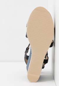 Sandale avec semelle beige texturée, brides noires et bleues à motif serpent, vue par le dessous sur fond blanc.