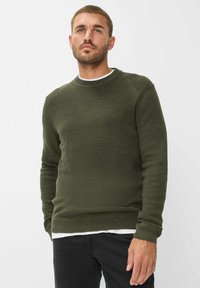 Maglione a maglia verde oliva con collo rotondo e texture a coste, dotato di maniche lunghe e orlo aderente, indossato sopra una camicia bianca.