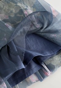 Transparente marineblaue Netzwebart mit Blumenmuster, auf einer soliden blauen Stoffbasis geschichtet. Weiche Textur mit sichtbaren Nahtdetails.