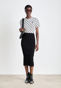 Bijela majica s crnim uzorkom "NY", rebrasta crna midi suknja i crne gležnjače s sjajnim detaljem na prstima, upotpunjeno sunčanim naočalama i torbom.