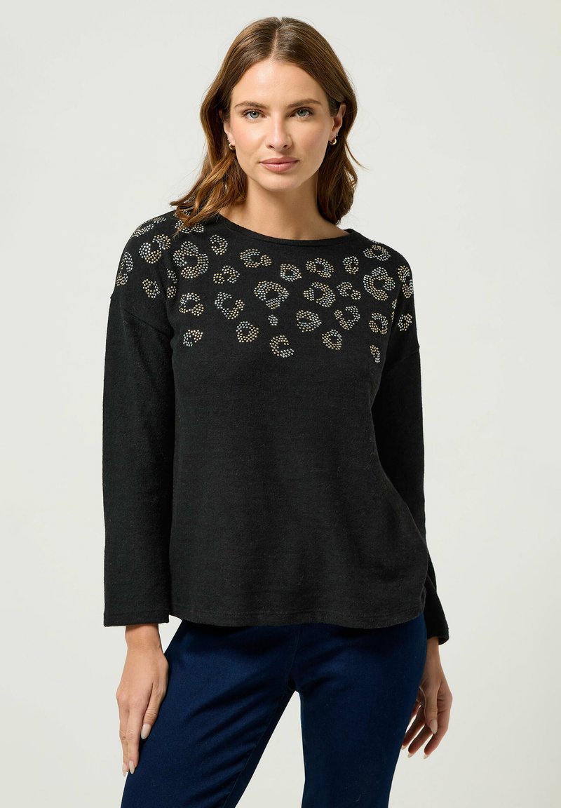 Schwarzer Pullover mit langen Ärmeln, der ein strukturiertes Tiermuster und goldene sowie silberne Nieten entlang des Ausschnitts aufweist. Weiches Material und entspannter Schnitt.