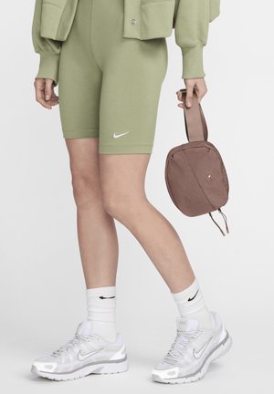 Zielone bawełniane szorty rowerowe, białe logo Nike, połączone z białymi sneakersami i prążkowanymi skarpetkami, trzymając brązową torbę z tkaniny z zamkiem błyskawicznym.