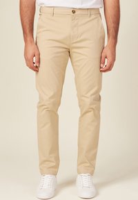 Chinos beige hechos de una mezcla de algodón, con un corte clásico, cremallera y bolsillos frontales. Combinados con zapatillas blancas.